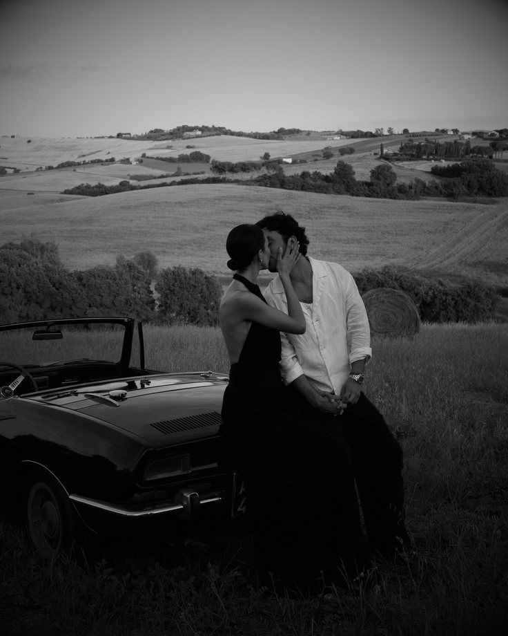 Pareja junto a un auto clásico en el campo, en blanco y negro